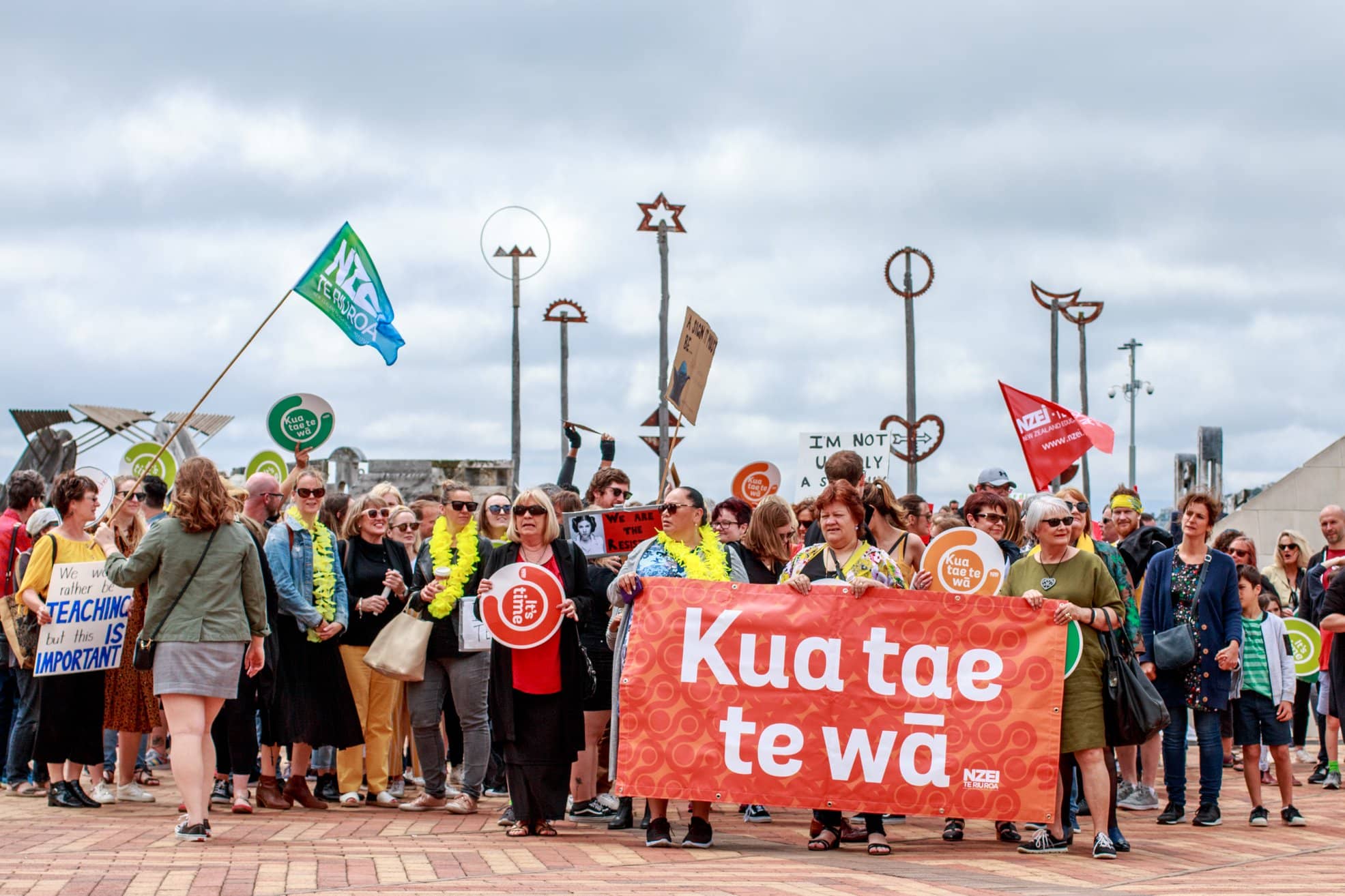 Many NZEI members gather on Wellington Waterfront with signs and a big banner reading Kua Tae Te Wā or Now is the Time